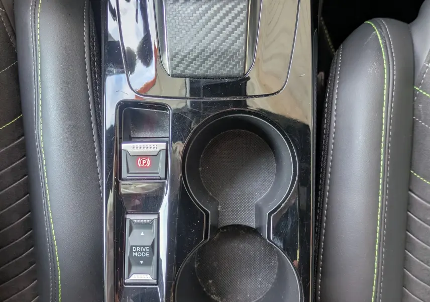 Vue plongeante sur la console centrale noire brillante de la Peugeot 208 Hybrid 145 GT avec surpiqûres vertes et commandes de boîte auto.