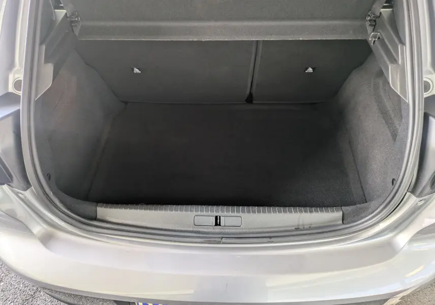 Coffre ouvert de la Peugeot 208 Hybrid 145 gris artense, vue arrière montrant l'espace de chargement vide.