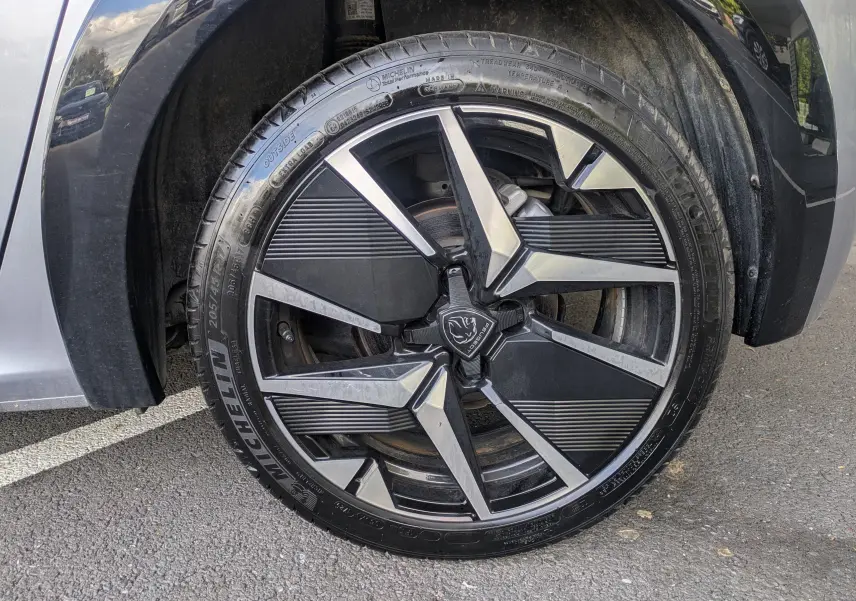 Gros plan sur la jante alliage 17'' bicolore noire et argent de la Peugeot 208 Hybrid 145 gris Artense, roue avant droite.