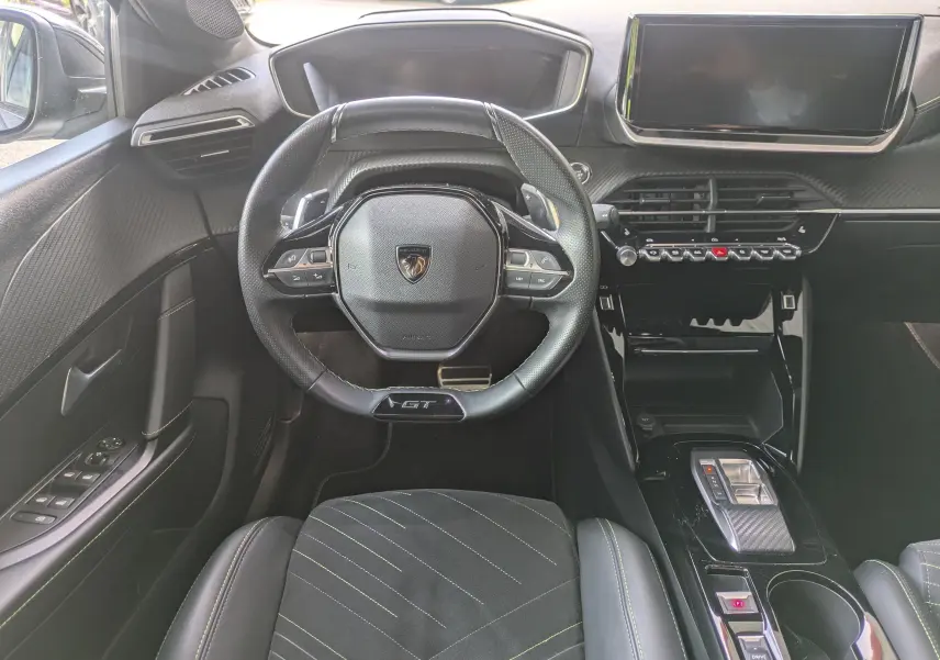 Vue intérieure frontale du poste de conduite de la Peugeot 208 Hybrid 145 GT avec volant GT et sellerie Alcantara noire surpiquée verte.