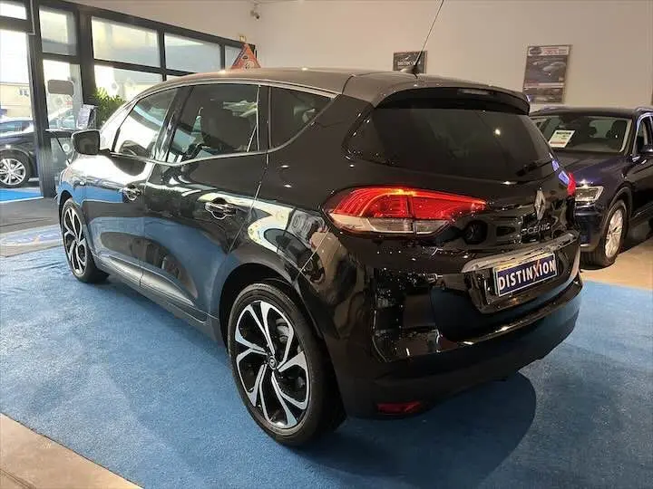 Vue 3/4 arrière droite d’un Renault Scénic IV noir étoile métal avec toit gris, en showroom sur moquette bleue.