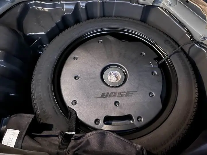 Gros plan sur la roue de secours et le caisson Bose noir dans le coffre d'un Renault Scenic IV noir étoile métal.