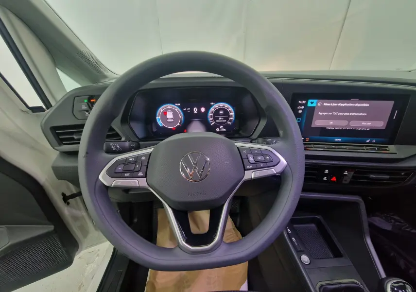 Vue centrée sur le volant et le tableau de bord numérique du Volkswagen Caddy Maxi blanc, mettant en valeur l'écran tactile et les commandes intégrées.
