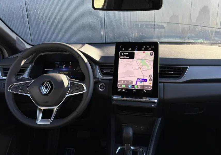 Vue intérieure du tableau de bord du Renault Captur 2025 avec volant noir et écran tactile vertical 10,4 pouces affichant la navigation.