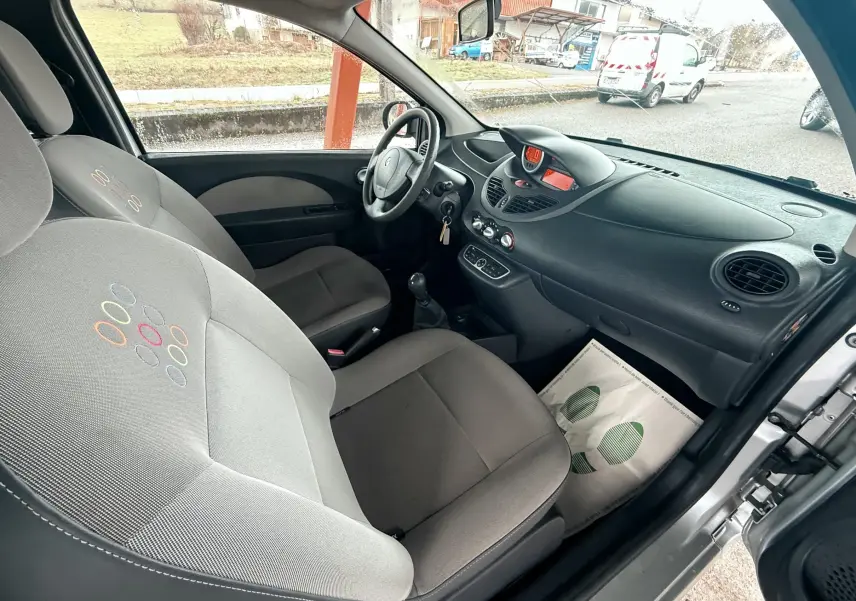 Vue intérieure côté conducteur de la Renault Twingo II grise de 2009 avec sièges tissu gris et volant cuir.