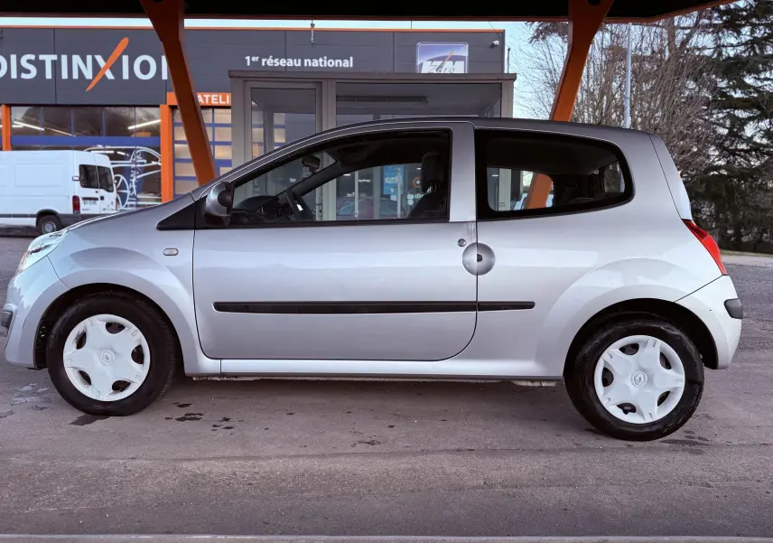 Profil côté gauche d'une Renault Twingo II grise 3 portes, avec jantes blanches et poignées noires visibles.