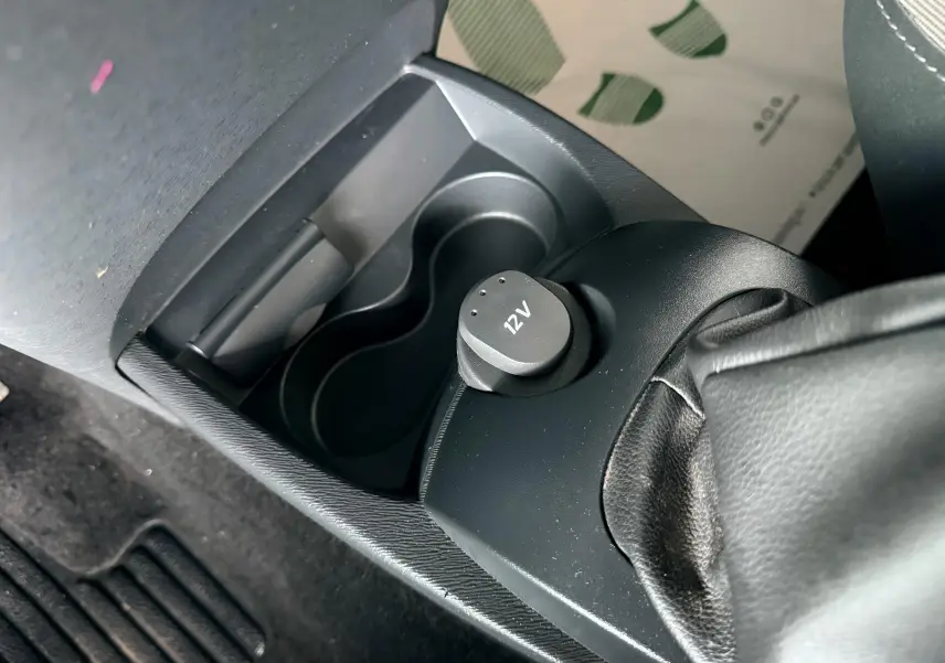 Gros plan sur la console centrale noire de la Renault Twingo II, avec prise 12V et frein à main en cuir visible.