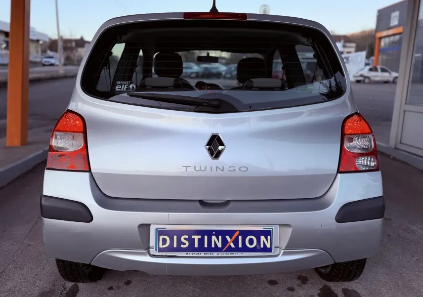 Vue arrière d’une Renault Twingo II gris clair de 2009, avec feux rouges et plaque d’immatriculation Distinxion.