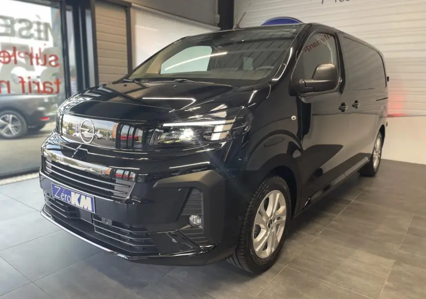 Vue 3/4 avant droit d'un Opel Vivaro noir carbone avec calandre chromée et phares allumés en showroom.