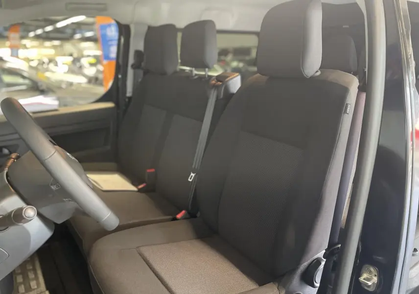 Vue intérieure côté conducteur de la cabine approfondie Opel Vivaro 2025 avec sièges tissu bi-ton noir/gris.