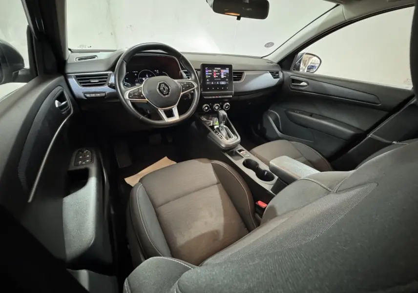 Vue intérieure avant droite du Renault Arkana Business E-TECH 145, tableau de bord noir avec écran tactile central et volant multifonctions.