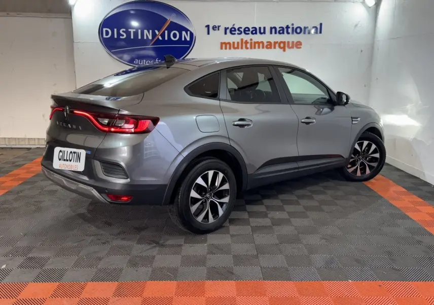 Vue 3/4 arrière droite d'une Renault Arkana Business E-TECH 145 gris foncé avec feux arrière LED allumés en intérieur showroom.