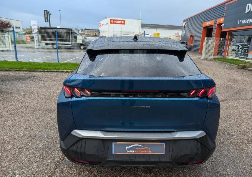 Vue arrière d’un Peugeot 3008 GT hybride bleu métallisé avec feux arrière à griffes LED et bandeau noir laqué.