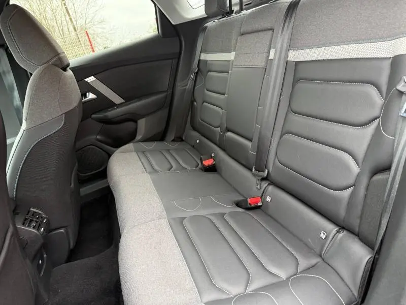 Vue intérieure arrière côté droit du Citroën C4 X 2024 avec sièges bi-matière gris et noir et ceintures de sécurité visibles.