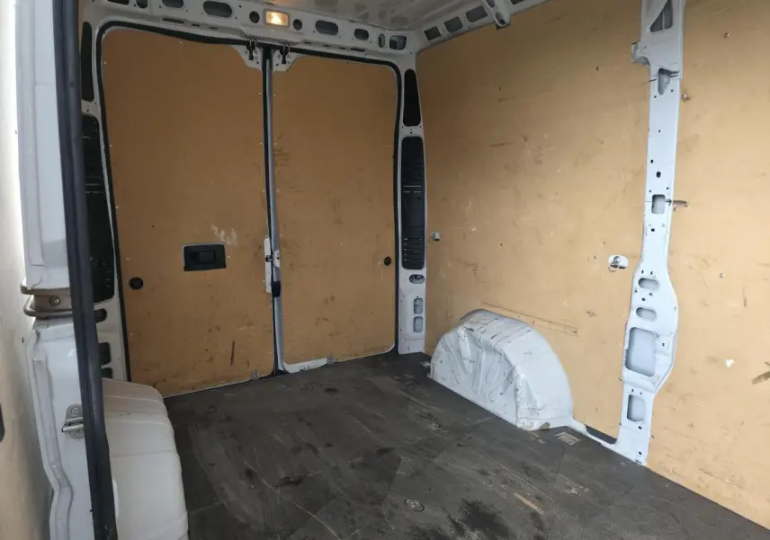 Vue intérieure arrière du fourgon blanc Opel Movano, montrant l'espace de chargement avec parois en bois et sol noir.