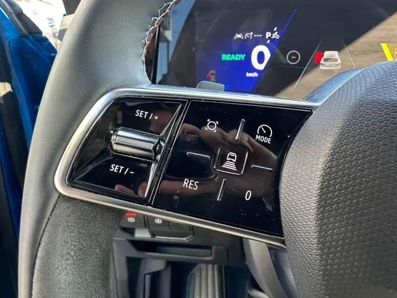 Gros plan sur les commandes du régulateur de vitesse au volant du Renault Rafale bleu sommet métallisé, avec affichage numérique en arrière-plan.