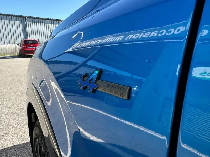 Gros plan sur l'aile avant gauche bleu sommet métallisé du Renault Rafale 1.2 E-Tech avec logo Esprit Alpine.