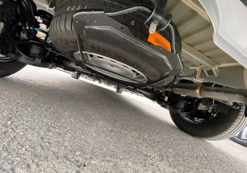 Vue sous le Citroën Berlingo blanc montrant la roue de secours suspendue sous le châssis et le système d'échappement.