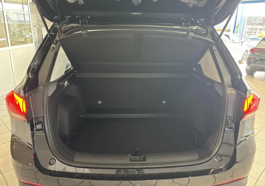 Coffre ouvert en vue arrière d’un MG Motor ZS 1.5 Hybrid+ noir, avec feux arrière allumés en intérieur showroom.