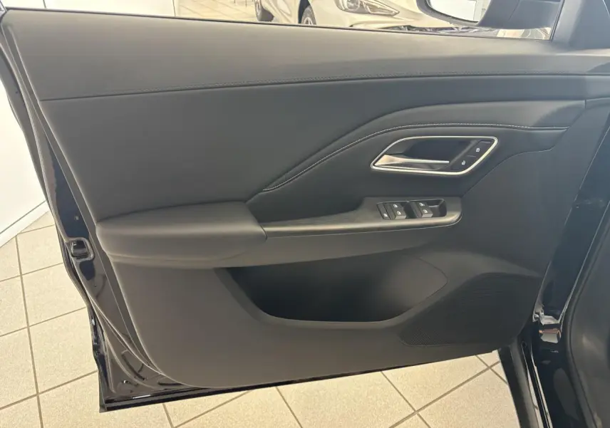 Porte avant gauche ouverte d’un MG MOTOR ZS 1.5 Hybrid+ noir, montrant les commandes de vitres et la poignée intérieure chromée.