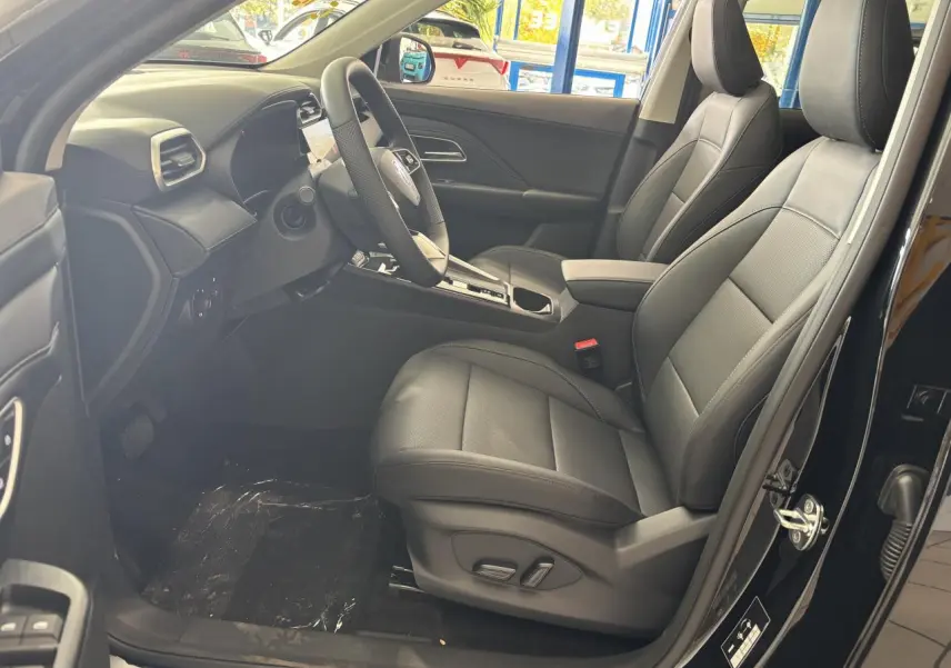 Vue intérieure côté conducteur du MG Motor ZS 1.5 Hybrid+ noir, sièges en tissu/similicuir noir et tableau de bord moderne.