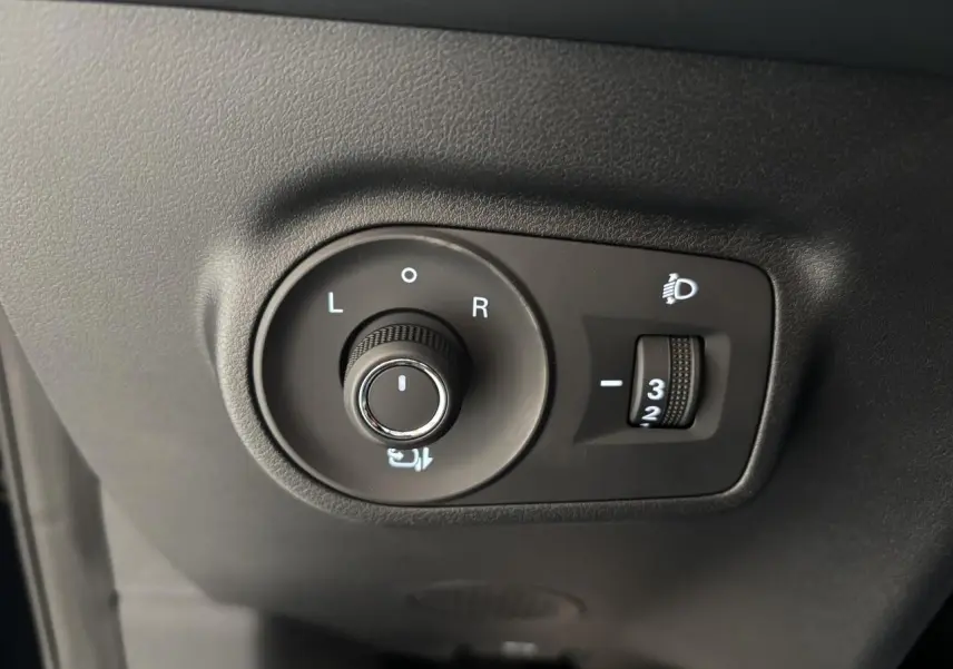 Gros plan sur les commandes de réglage des rétroviseurs et des phares du MG Motor ZS 1.5 Hybrid+ noir, côté conducteur.