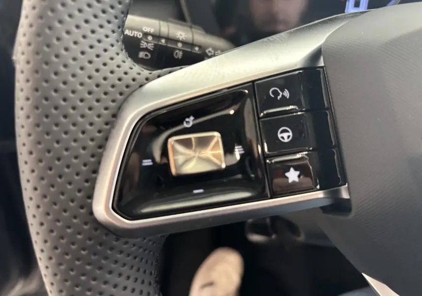 Gros plan sur les commandes multifonctions gauche du volant perforé noir du MG Motor ZS 1.5 Hybrid+ 2026.