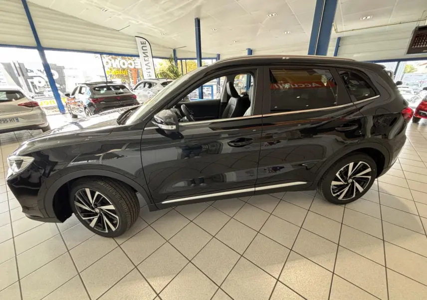 Vue de profil côté gauche du MG ZS 1.5 Hybrid+ noir, avec jantes alliage et intérieur visible en concession.