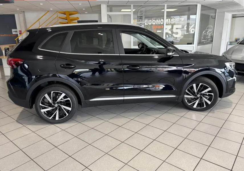 Vue de profil côté gauche du SUV MG ZS 1.5 Hybrid+ noir brillant, avec jantes alliage 18 pouces en concession.