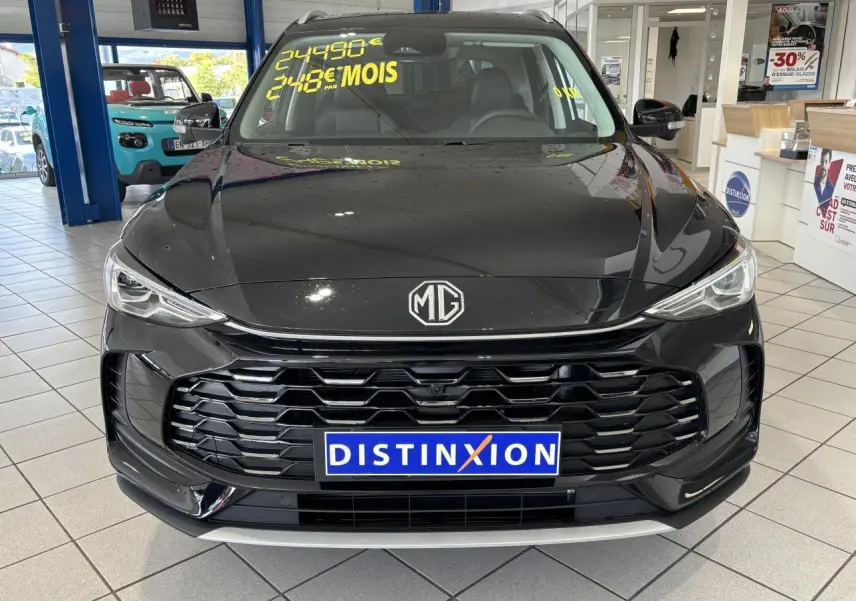 Vue avant d’un MG Motor ZS 1.5 Hybrid+ noir 2026 en showroom avec calandre hexagonale et logo MG visible.