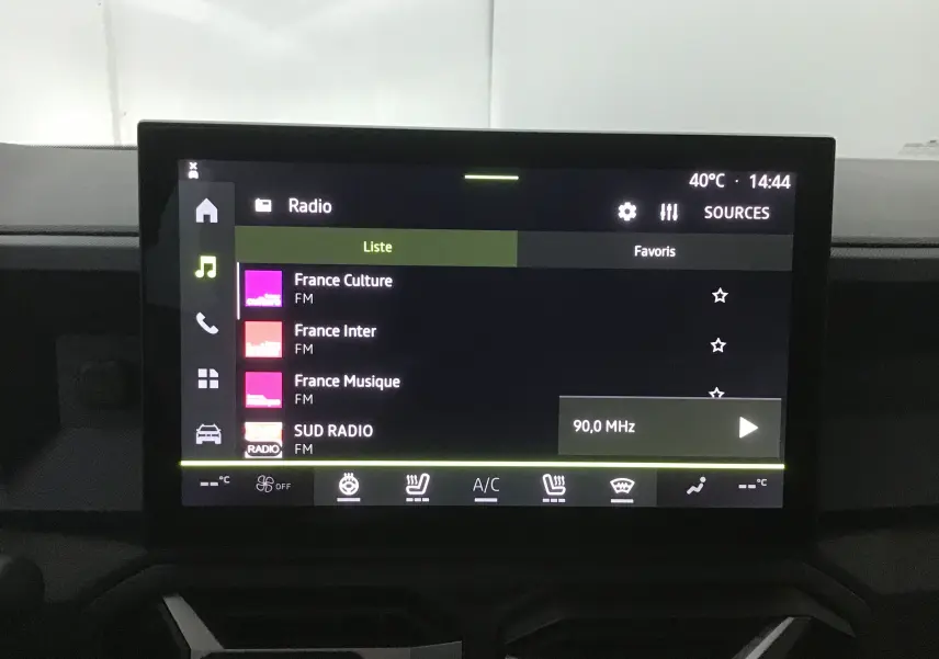 Écran tactile central du tableau de bord du Dacia Bigster gris schiste, affichant les stations radio FM et commandes climatisation.