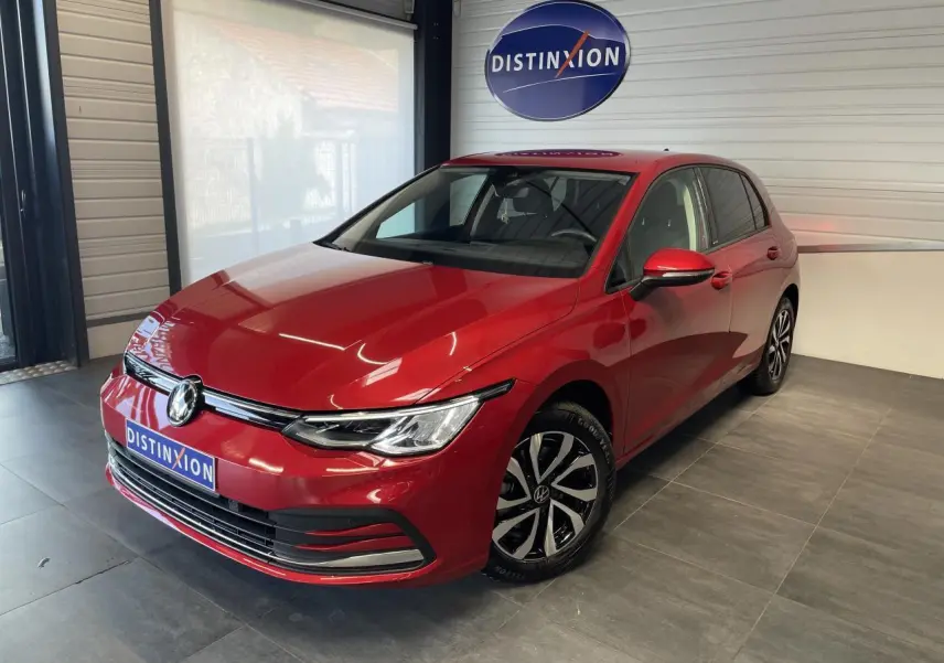 Vue 3/4 avant droite d'une Volkswagen Golf rouge métal avec jantes alliage et logo VW visible sur le capot.