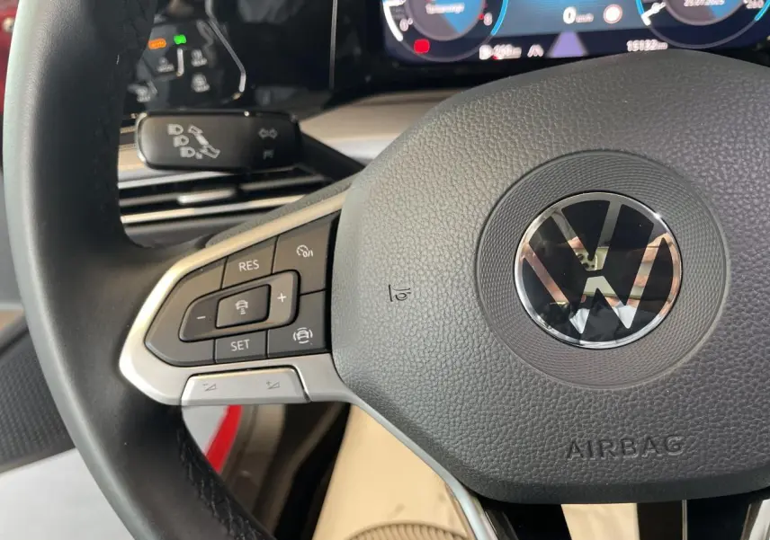 Gros plan sur le volant multifonction noir de la Volkswagen Golf 1.5 TSI Active rouge métal, avec tableau de bord digital en arrière-plan.