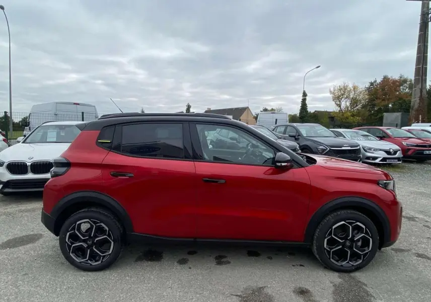Profil côté gauche d'une Citroën C3 2025 rouge Elixir avec toit noir et jantes alliage 17 pouces sur parking.