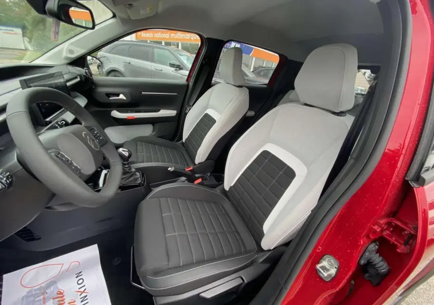 Intérieur avant de la Citroën C3 rouge Elixir, sièges bicolores gris et noir, volant et tableau de bord visibles.
