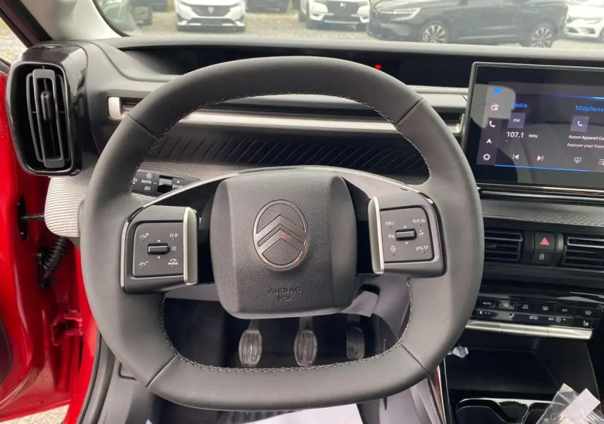 Vue intérieure centrée sur le volant carré du Citroën C3 rouge Elixir avec tableau de bord et écran tactile visible.