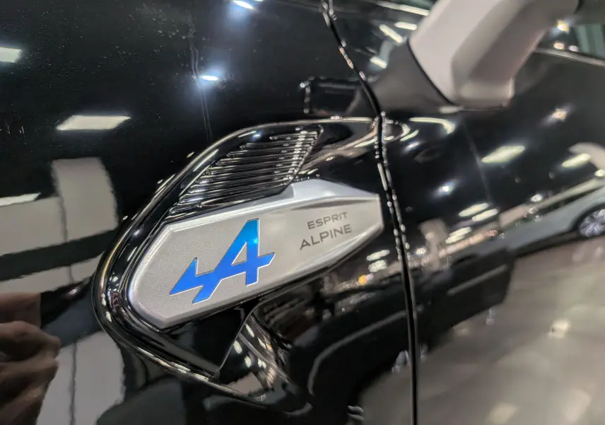 Gros plan sur l'emblème bleu "Esprit Alpine" sur la portière noire étoilée du Renault Captur hybride 2025.