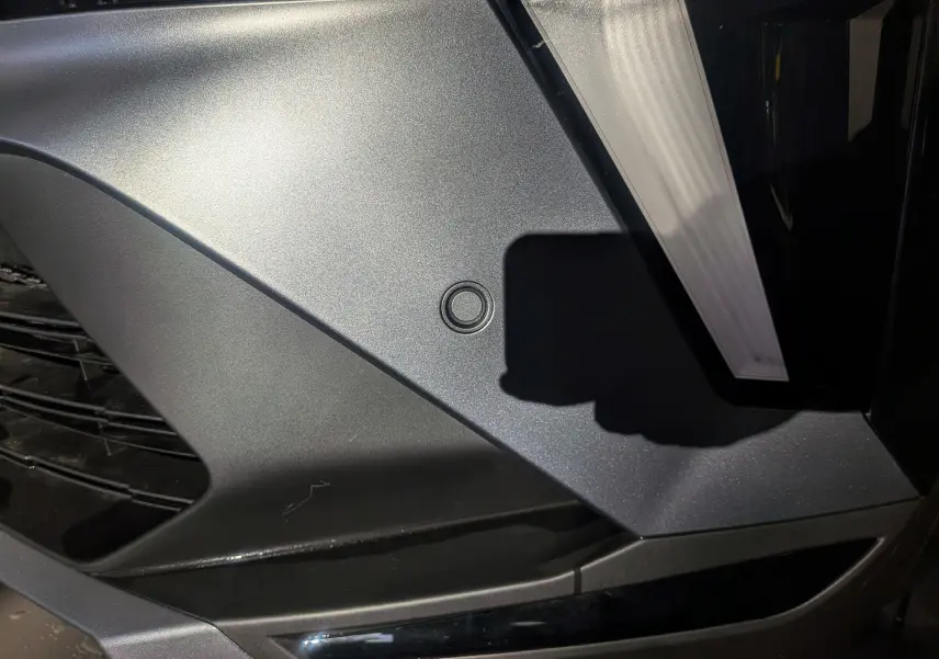 Gros plan sur le pare-chocs avant noir étoilé du Renault Captur E-TECH Full Hybrid 160 CH esprit Alpine, avec capteur de stationnement visible.