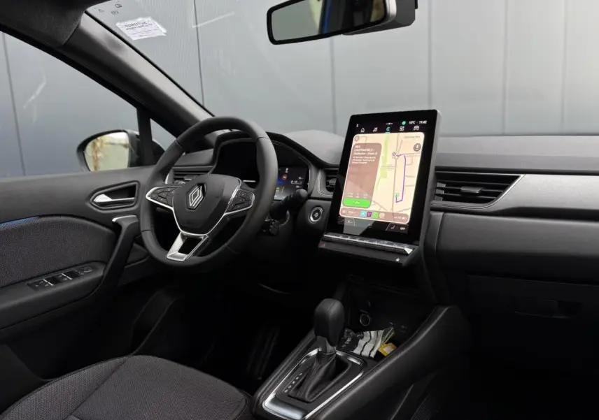 Vue intérieure côté conducteur du Renault Captur bleu Iron 2025, avec écran tactile vertical et volant multifonction.