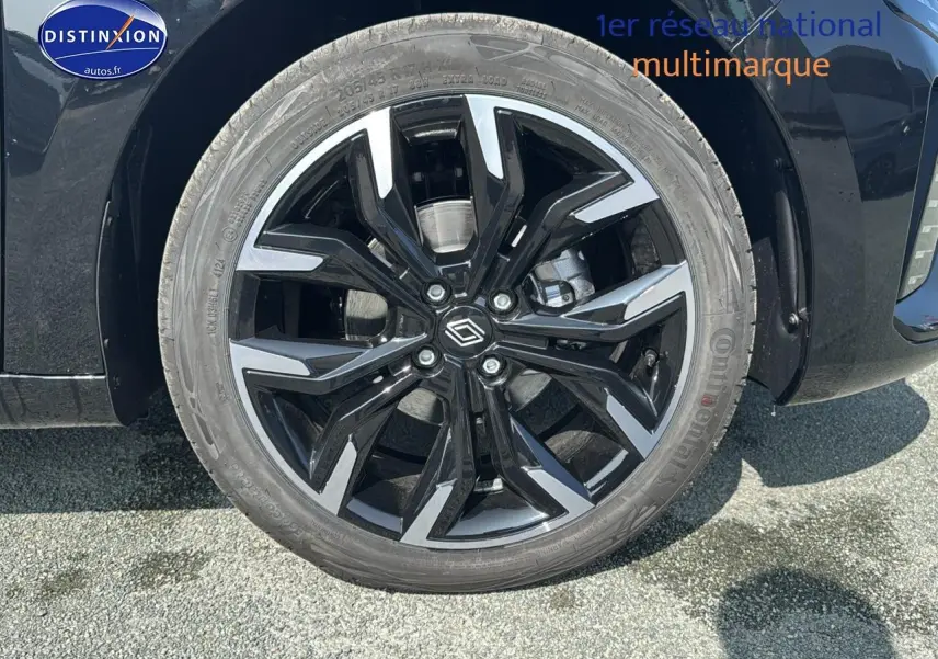 Gros plan sur la jante alu noire et argentée côté gauche d'une Renault Clio V noire, avec logo central distinctif.