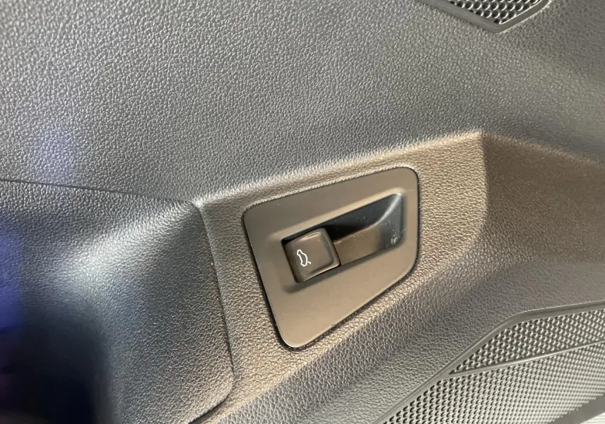 Gros plan sur le bouton d'ouverture électrique du hayon dans l'habitacle noir du Volkswagen Touareg blanc.