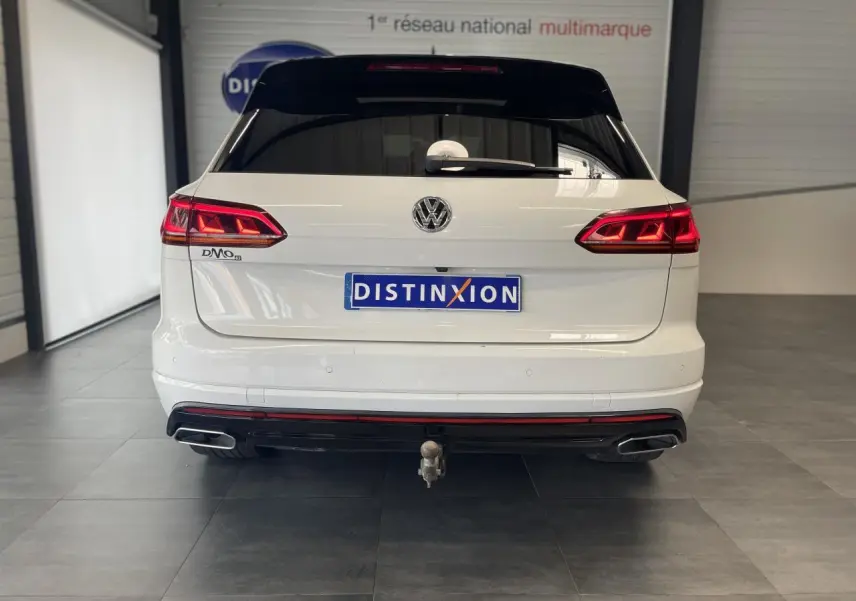 Vue arrière d'un Volkswagen Touareg blanc avec feux LED, double sortie d'échappement et attelage visible en intérieur showroom.