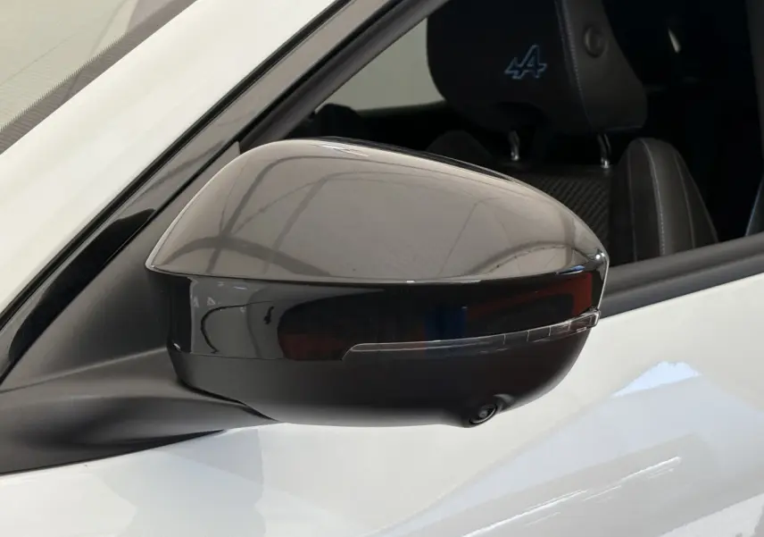 Rétroviseur droit noir brillant d’un Renault Espace blanc esprit Alpine, avec logo Alpine visible sur l’appui-tête.