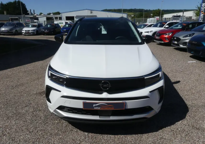 Vue avant d'un Opel Grandland blanc métallisé avec calandre noire brillante et phares LED, sur un parking extérieur.