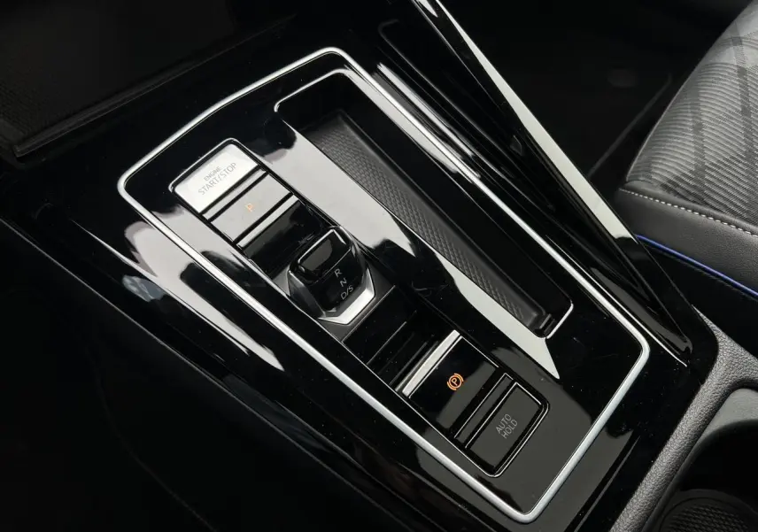 Vue rapprochée de la console centrale noire brillante de la Volkswagen Golf VIII R-Line avec sélecteur de boîte automatique et bouton start/stop.