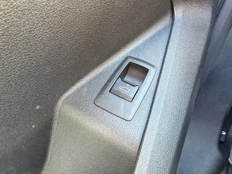 Gros plan sur le bouton d'ouverture du coffre côté intérieur d'une BMW Série 1 120dA M Sport gris Brooklyn métallisé.