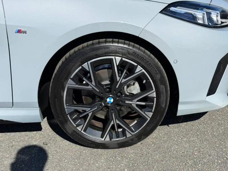 Gros plan sur la roue avant droite d'une BMW Série 1 M Sport 120dA en M Brooklyn Grey métallisé avec jante alu noire et grise.
