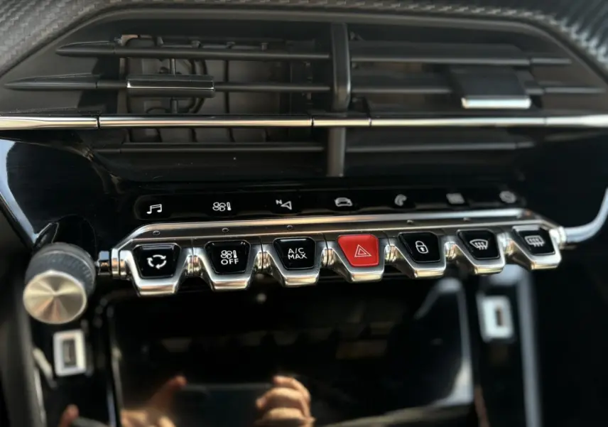 Gros plan sur la console centrale noire du Peugeot 2008 GT 2021, mettant en valeur les commandes chromées et un bouton rouge d’alerte.