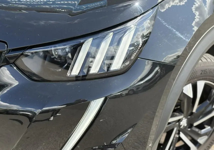 Gros plan sur le phare avant droit et la jante alliage 17'' noir Onyx du Peugeot 2008 GT noir métallisé.