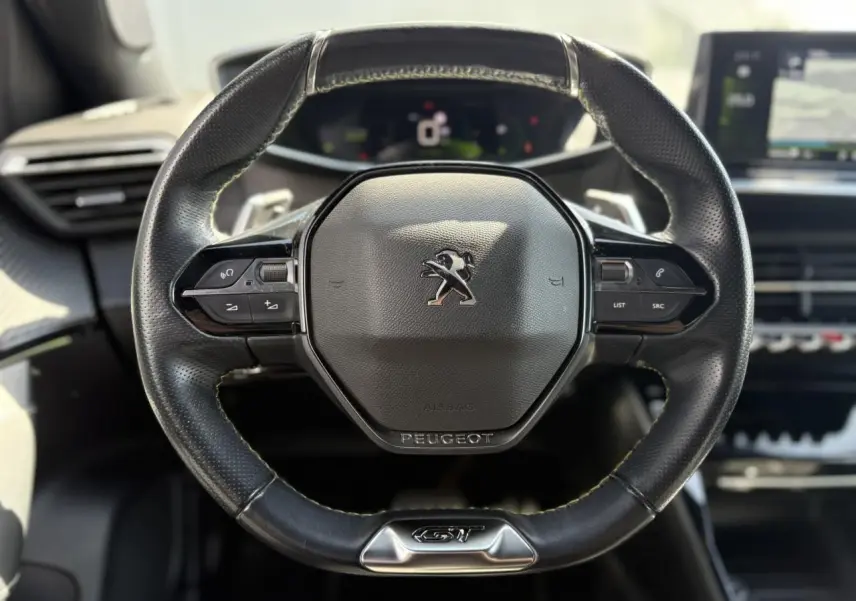 Volant cuir noir Peugeot 2008 GT vu de face avec commandes intégrées et badge GT chromé en bas.